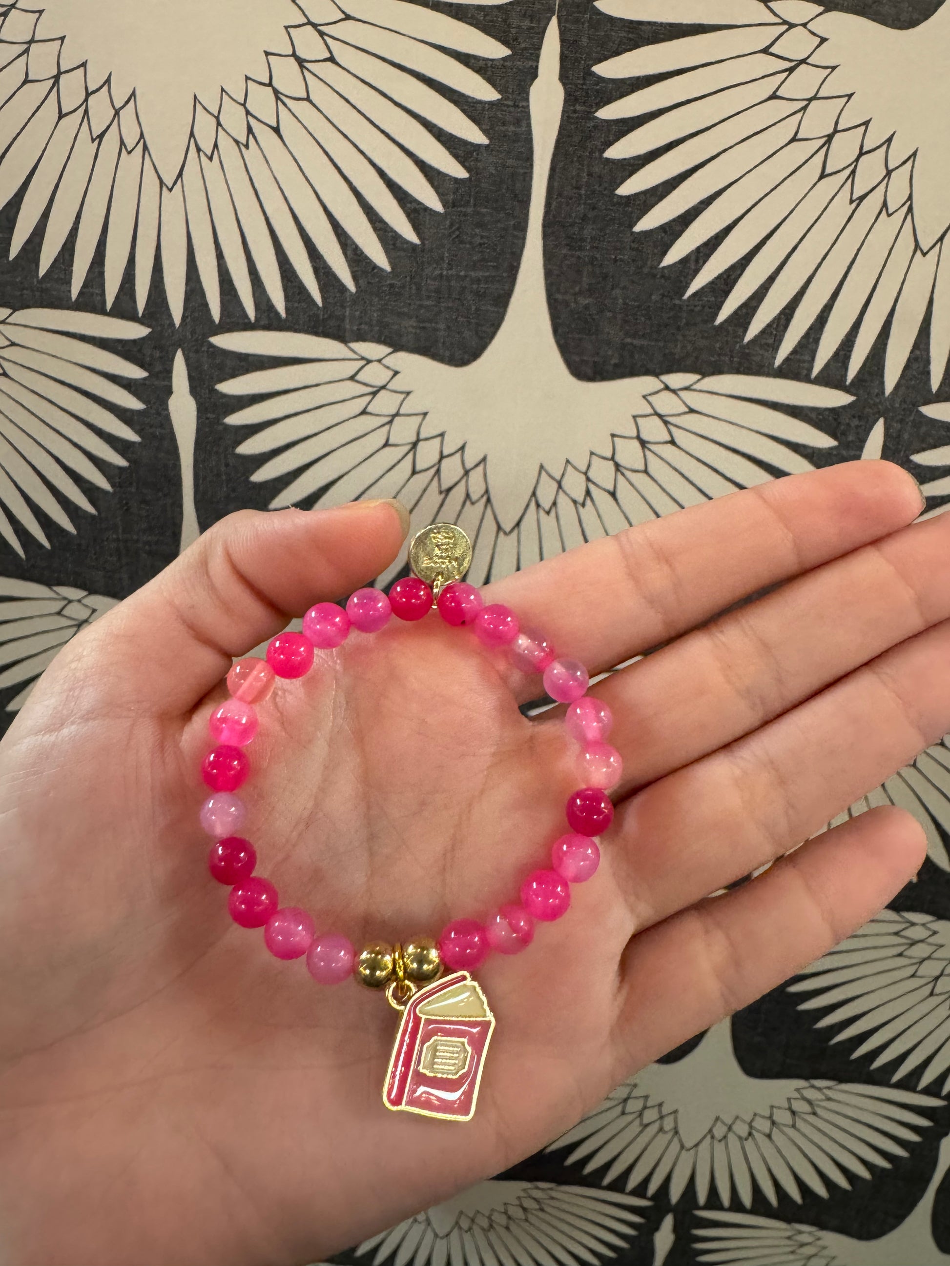 Pink beaded stretch bracelet with gold book charm and small coin charm