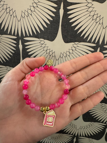 Pink beaded stretch bracelet with gold book charm and small coin charm