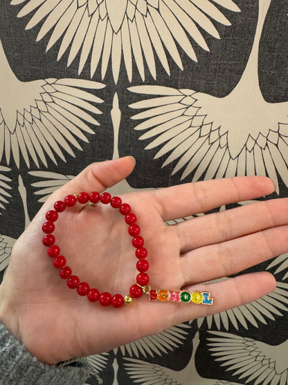 Red beaded stretch bracelet with colorful enamel letter charms spelling SCHOOL