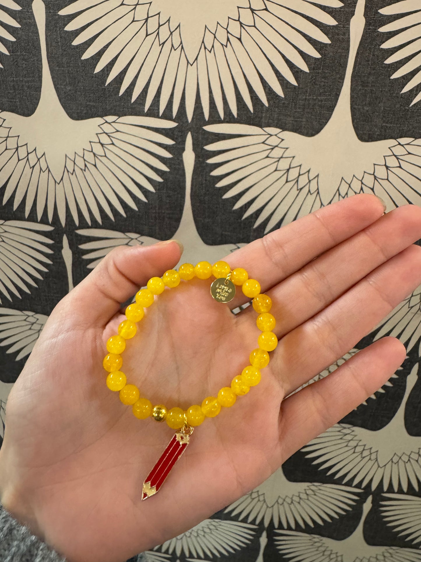 Yellow beaded stretch bracelet with red and gold pencil charm and small gold disc