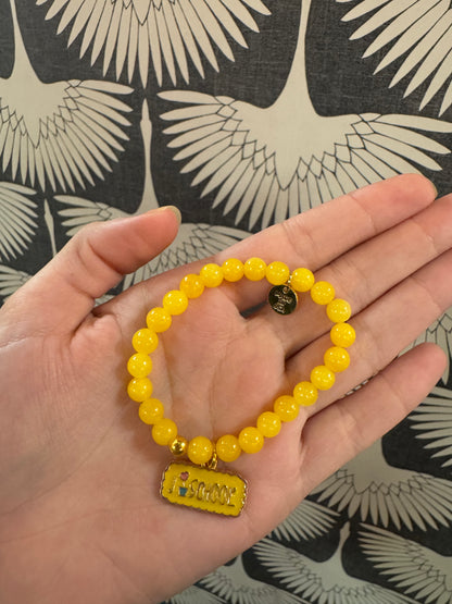 Yellow beaded stretch bracelet with gold "I Love School" enamel charm, held in palm