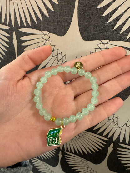 Light green beaded bracelet with enamel book charm held in open palm