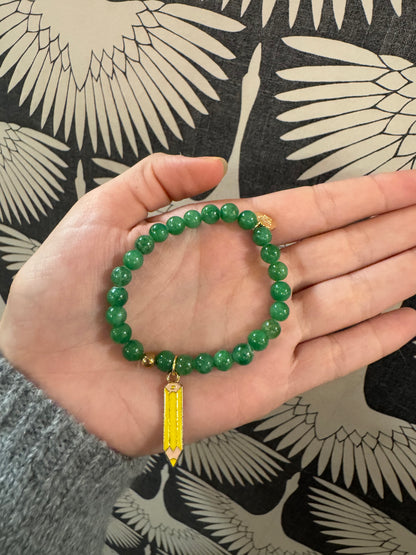 Green beaded stretch bracelet with yellow enamel pencil charm and gold accents