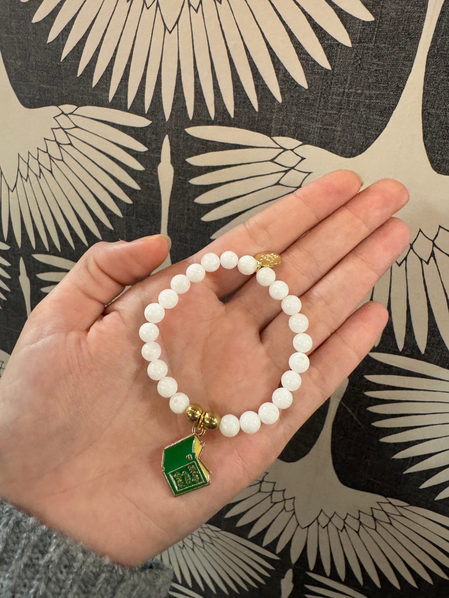 White beaded stretch bracelet with green and gold enamel school house charm