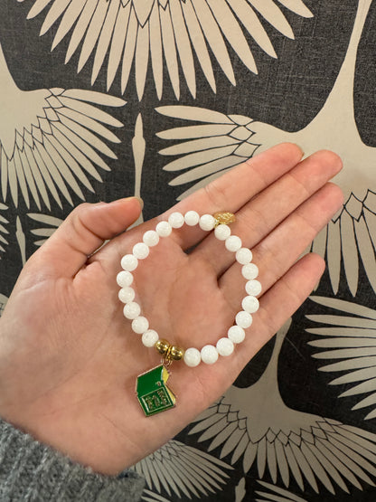 White beaded stretch bracelet with green and gold enamel school house charm
