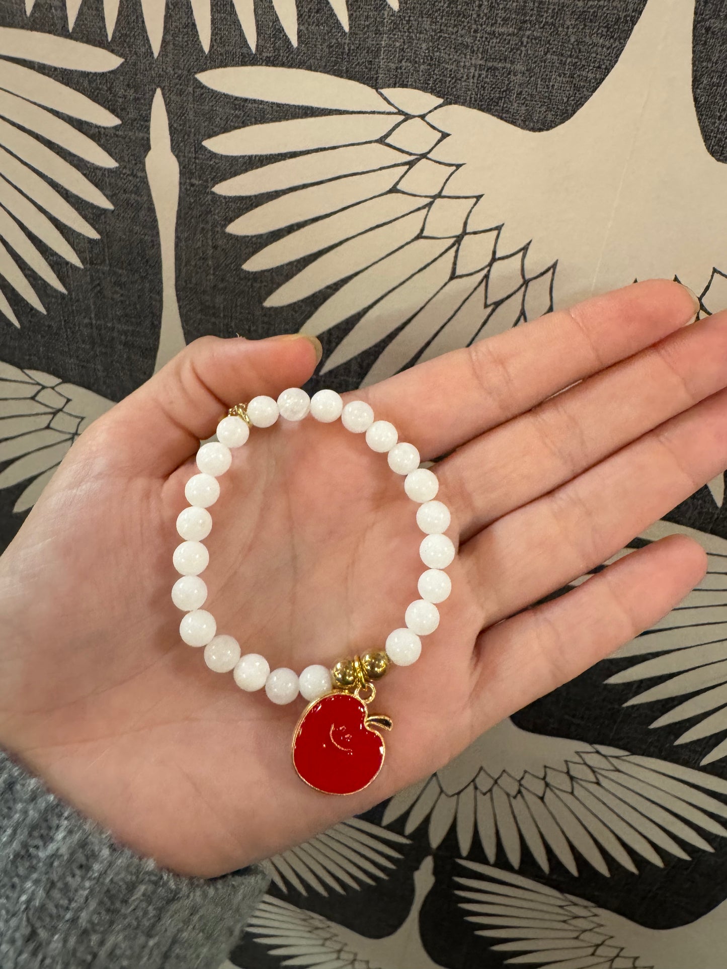 White beaded stretch bracelet with red enamel apple charm and gold accents