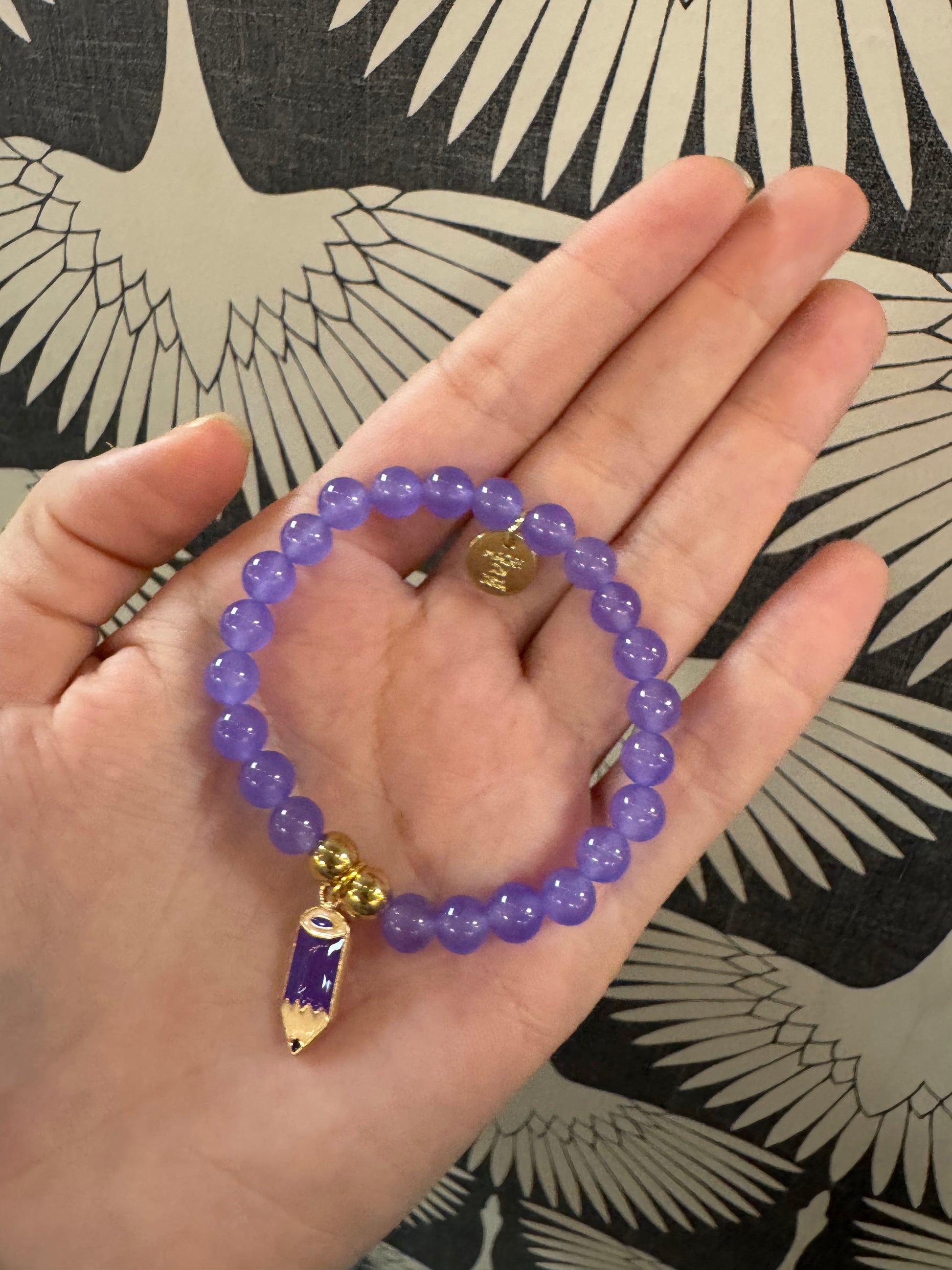 Purple beaded stretch bracelet with gold charm pendant featuring purple enamel and eye detail
