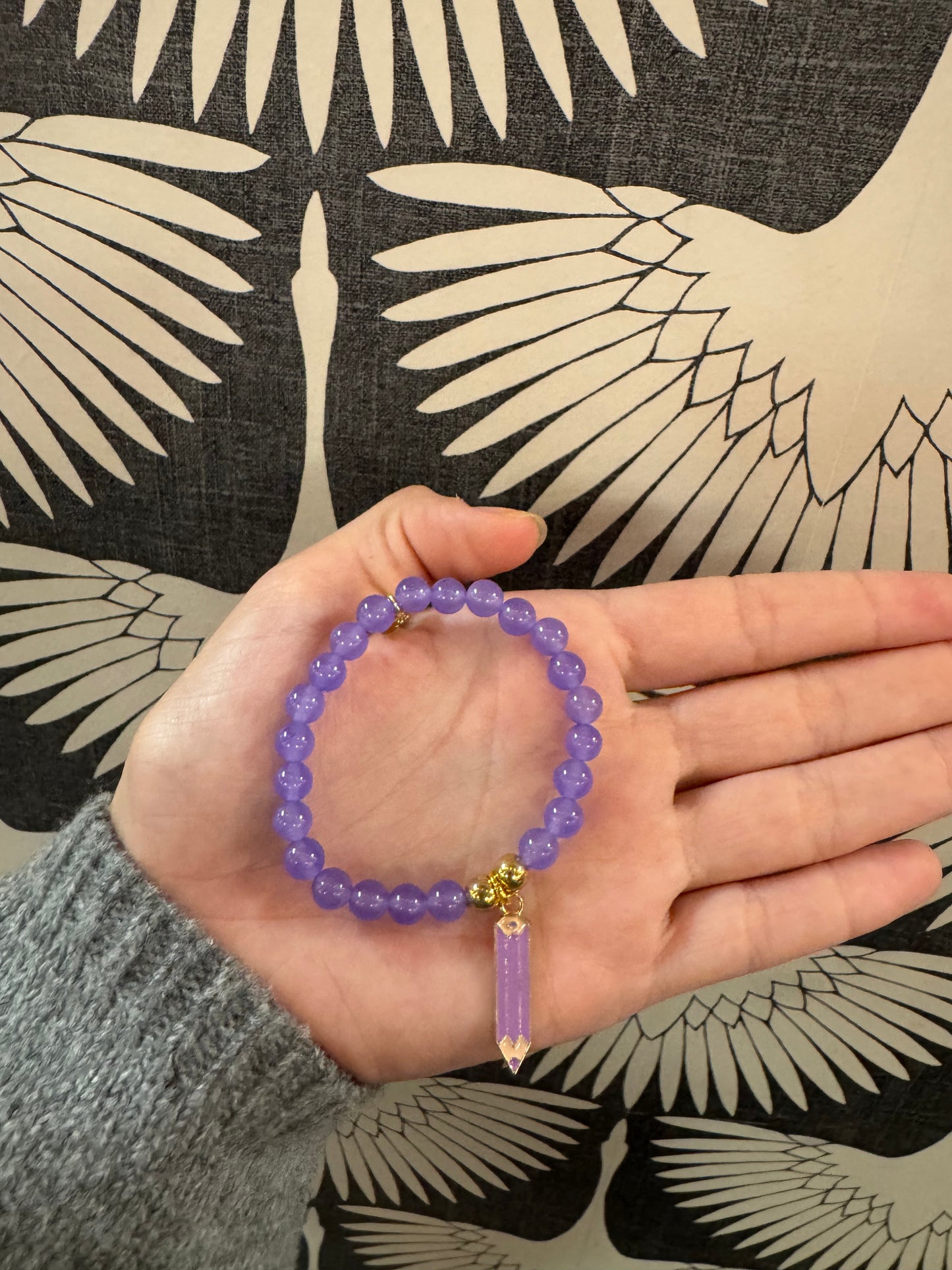 Purple beaded stretch bracelet with gold accents and a dangling crystal point charm