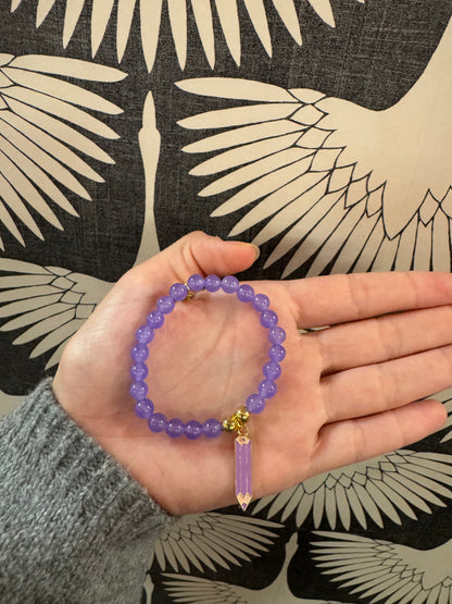 Purple beaded stretch bracelet with gold accents and a dangling crystal point charm