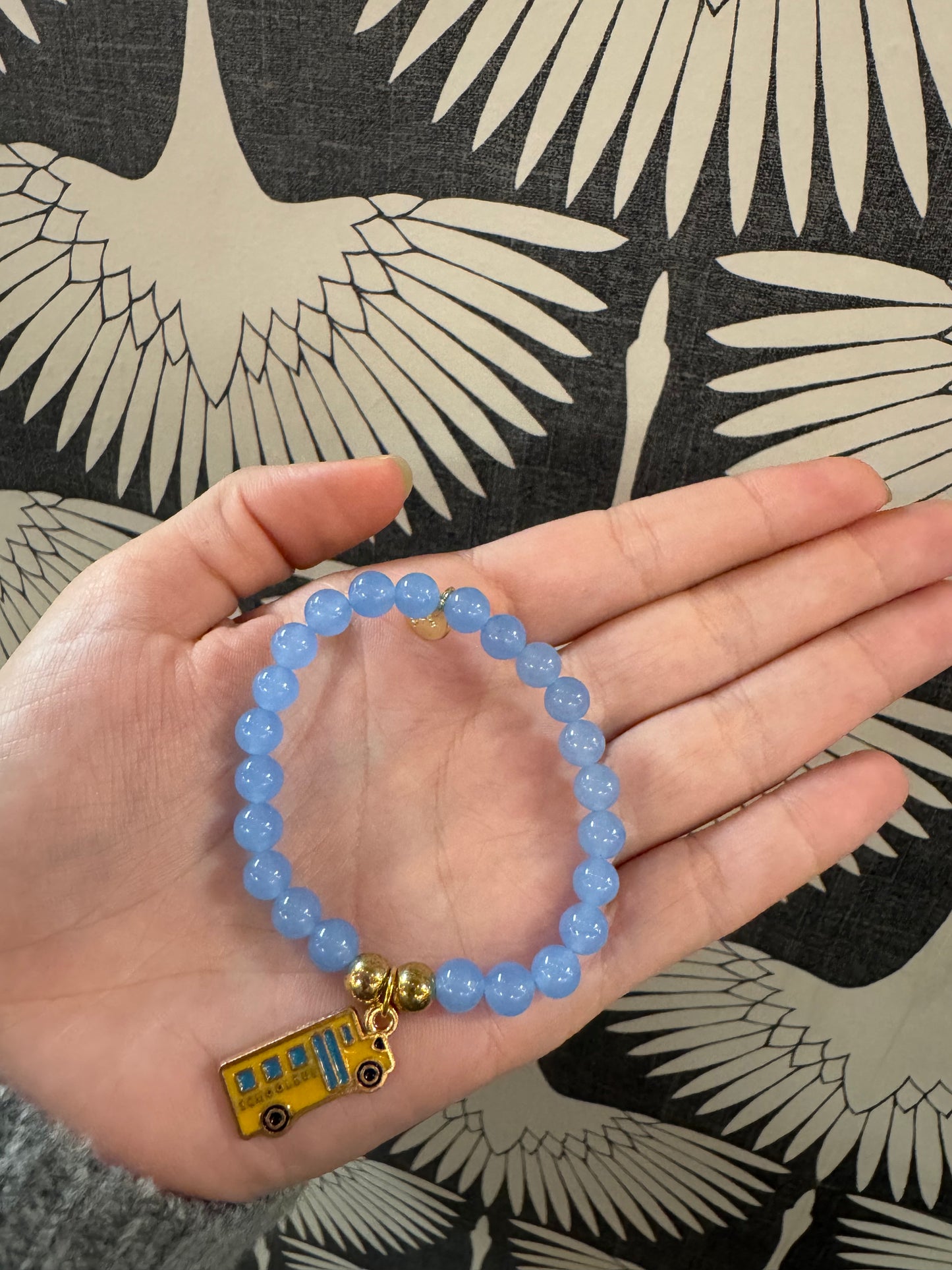Blue beaded stretch bracelet with a yellow enamel school bus charm held in palm