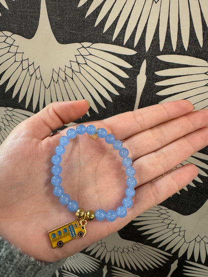 Blue beaded stretch bracelet with a yellow enamel school bus charm held in palm