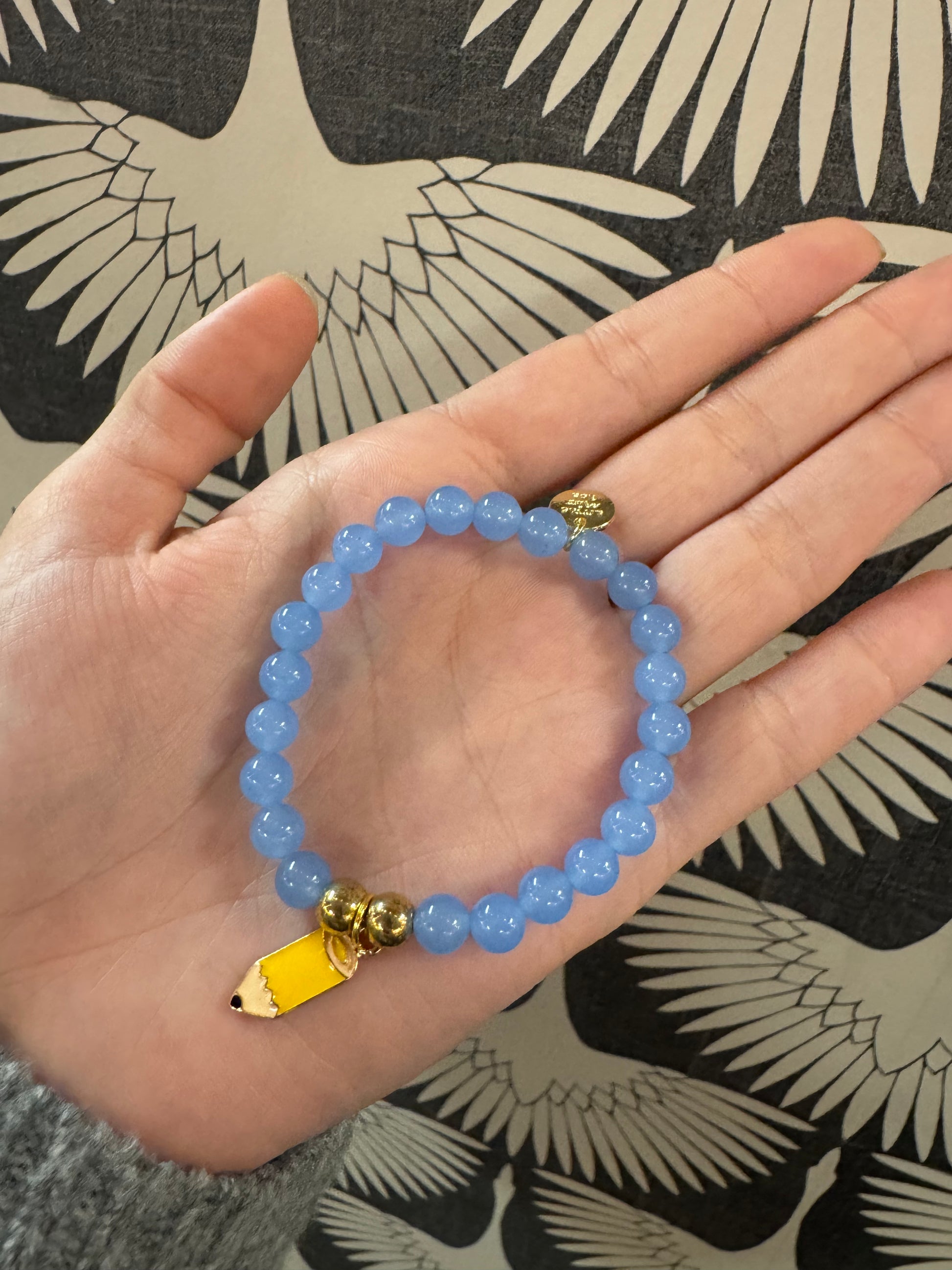 Blue beaded stretch bracelet with yellow pencil charm and gold accent beads