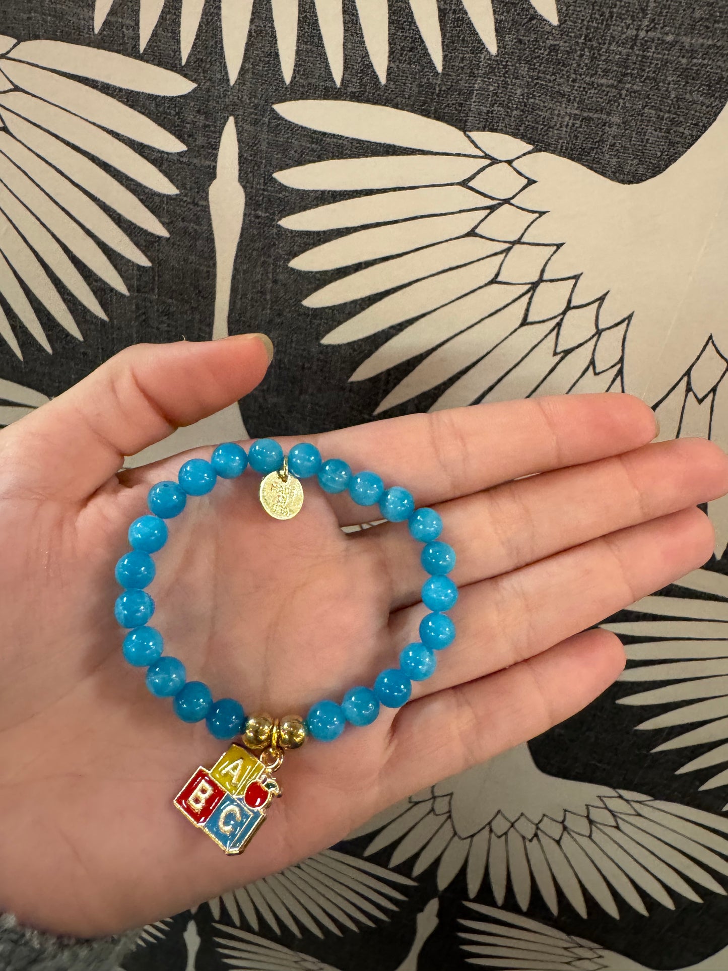 Blue beaded stretch bracelet with colorful ABC block charm and gold coin pendant