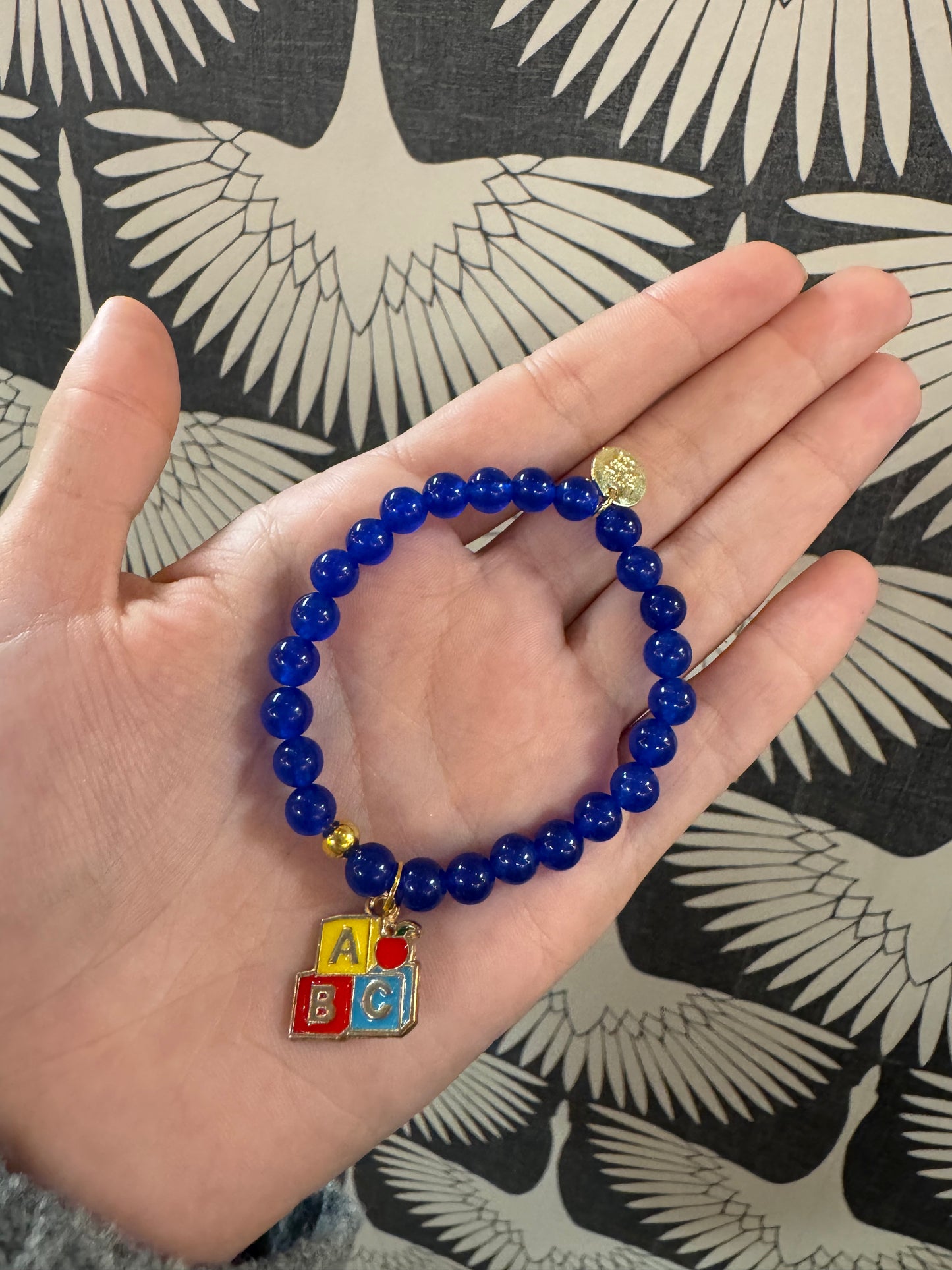 Blue beaded stretch bracelet with colorful ABC blocks enamel charm, held in palm