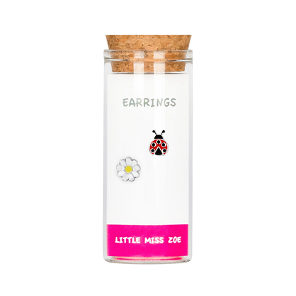 Glass bottle with cork lid containing ladybug and daisy stud earrings, pink base label
