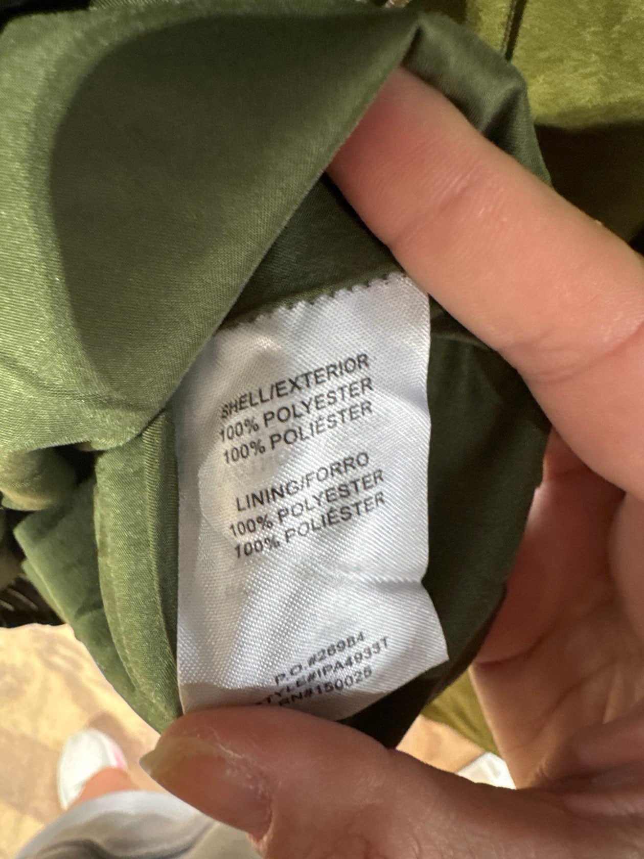 Green polyester garment interior label showing shell and lining fabric content details