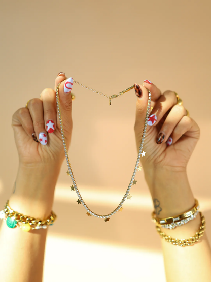 Gold crystal tennis necklace with dangling star charms held up by two hands
