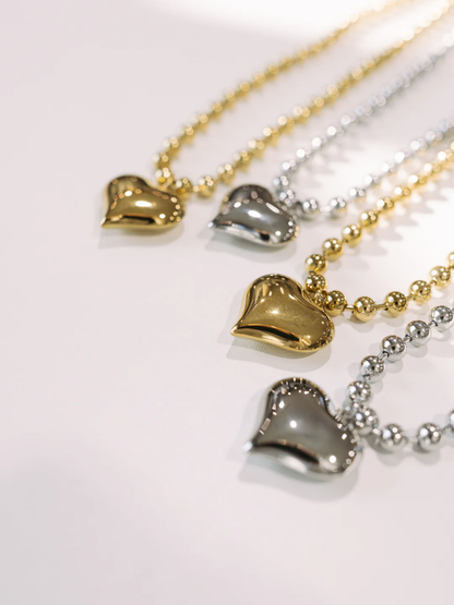 Four puffy heart pendant beaded necklaces in gold and silver tones on white surface.