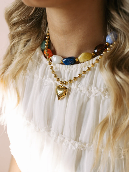 Gold beaded necklace with colorful stones and heart pendant on white top