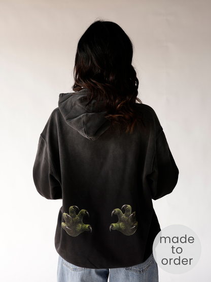 Back view of black oversized hoodie with green dinosaur claw prints at hem