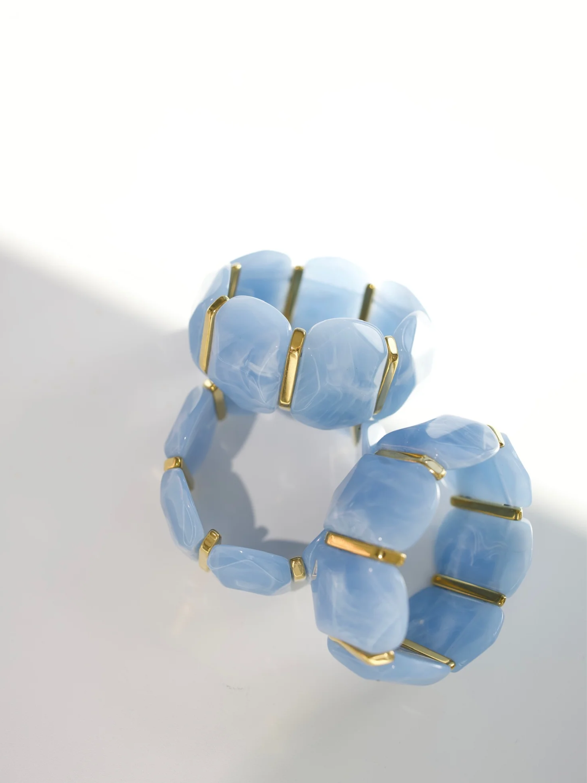 Light blue marbled stretch bracelet with gold-tone bar spacers between rounded tiles