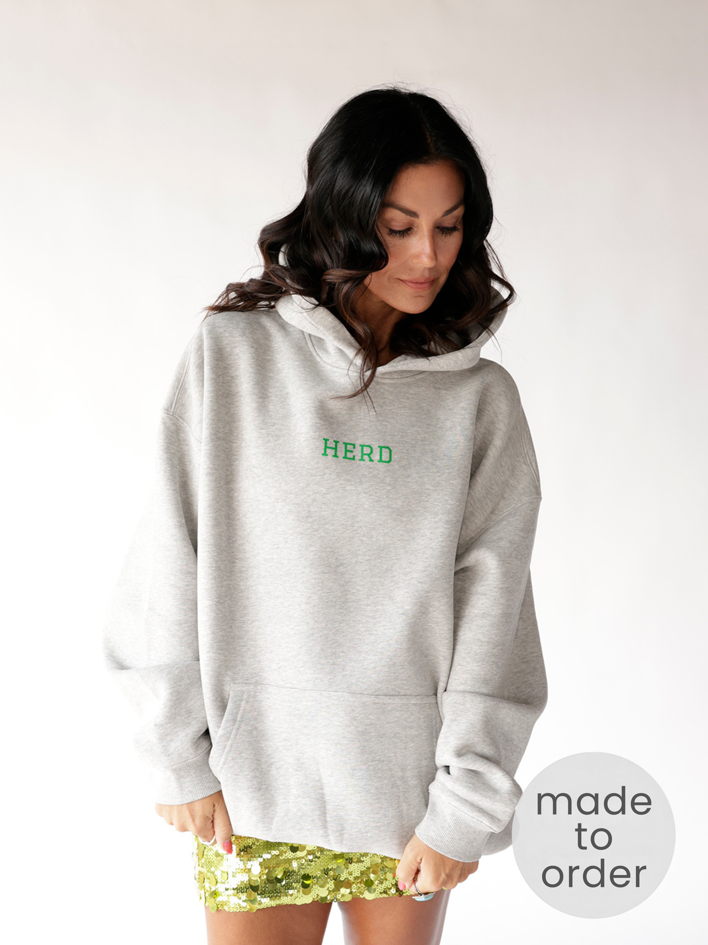 Oversized grey hoodie with green HERD embroidery, paired with gold sequin mini skirt