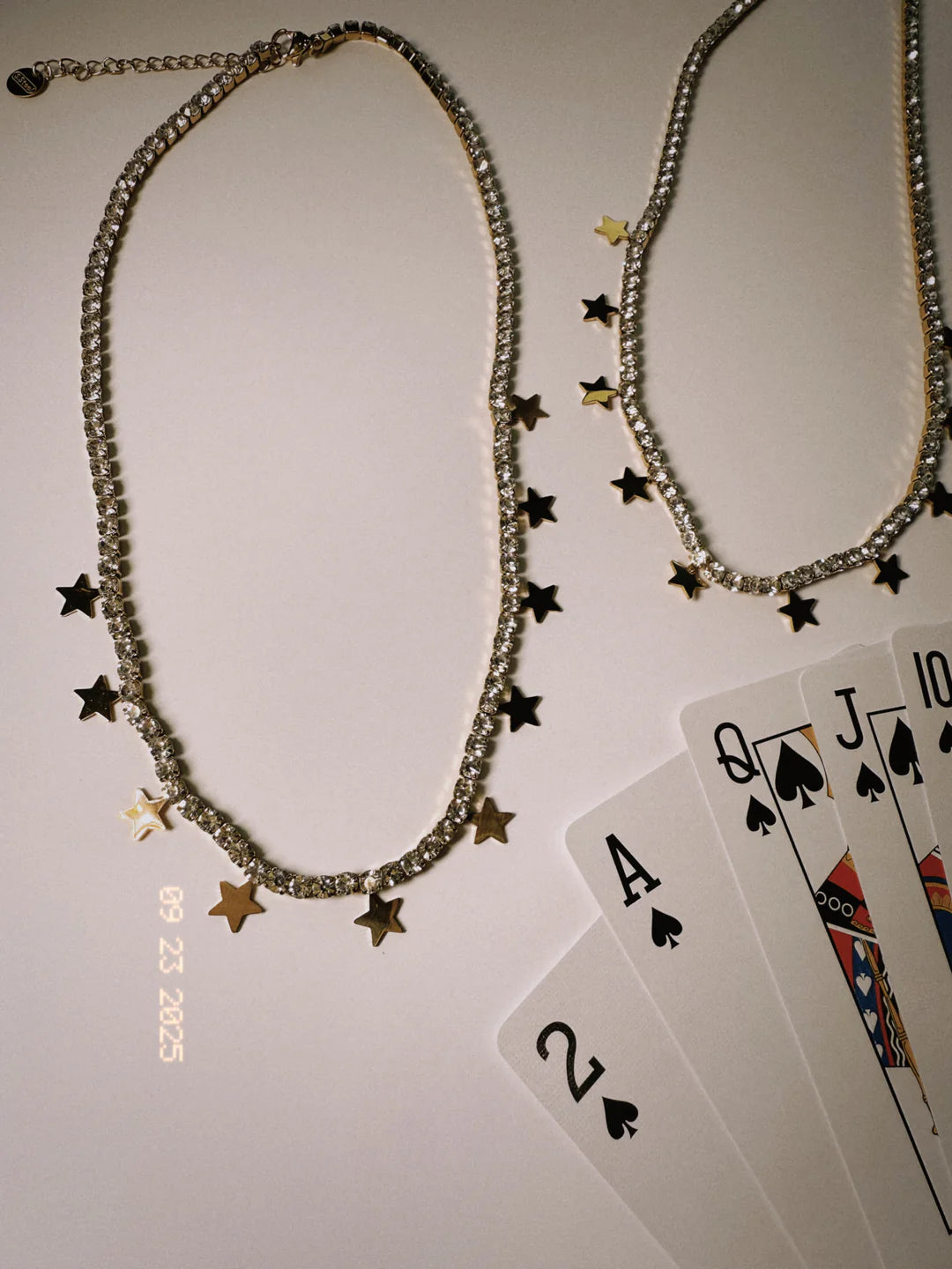 Crystal tennis necklace with mixed gold and black star charms, styled with playing cards